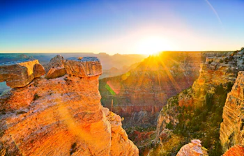 Spektakulær solnedgang over Grand Canyon med gyldent lys på røde klippeformationer i Arizona