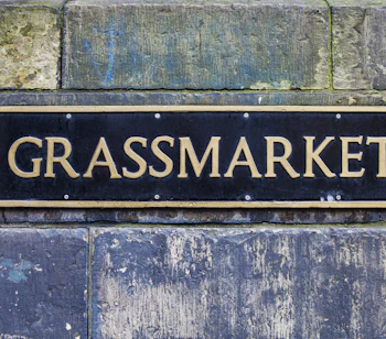 Sort og guldfarvet gadeskilt for Grassmarket monteret på historisk stenmur i Edinburgh, Skotland