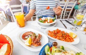 Person der nyder friskgrillet middelhavsretter med rejer og blæksprutte serveret med grøntsagssalat i Grækenland