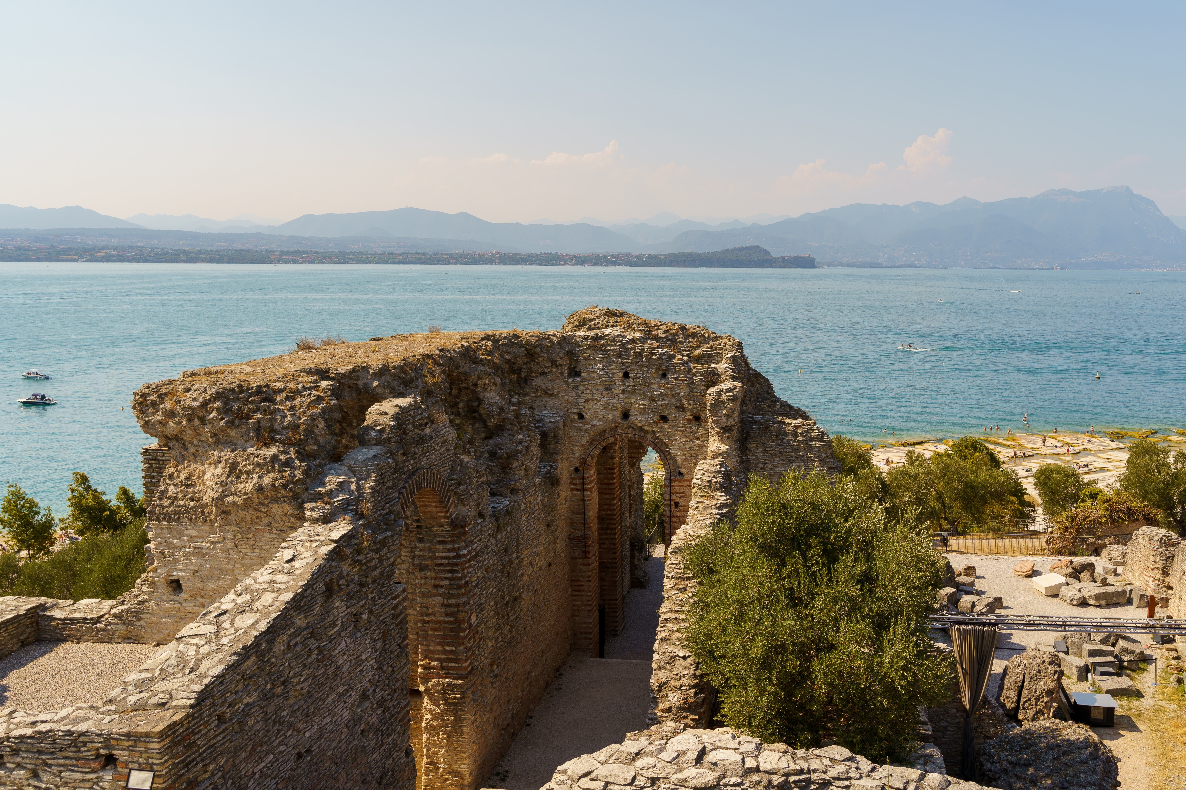 Historiske ruiner fra Grotte di Catullo i Sirmione med udsigt over Gardasøens azurblå vand og bjerglandskab. Resterne af den romerske villa vidner om områdets rige historie