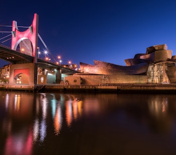 Guggenheim-museet i Bilbao oplyst om aftenen med den karakteristiske arkitektur spejlet i floden Ria de Bilbao