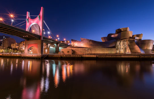 Guggenheim-museet i Bilbao oplyst om aftenen med den karakteristiske arkitektur spejlet i floden Ria de Bilbao