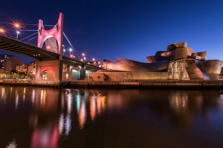 Guggenheim-museet i Bilbao oplyst om aftenen med den karakteristiske arkitektur spejlet i floden Ria de Bilbao