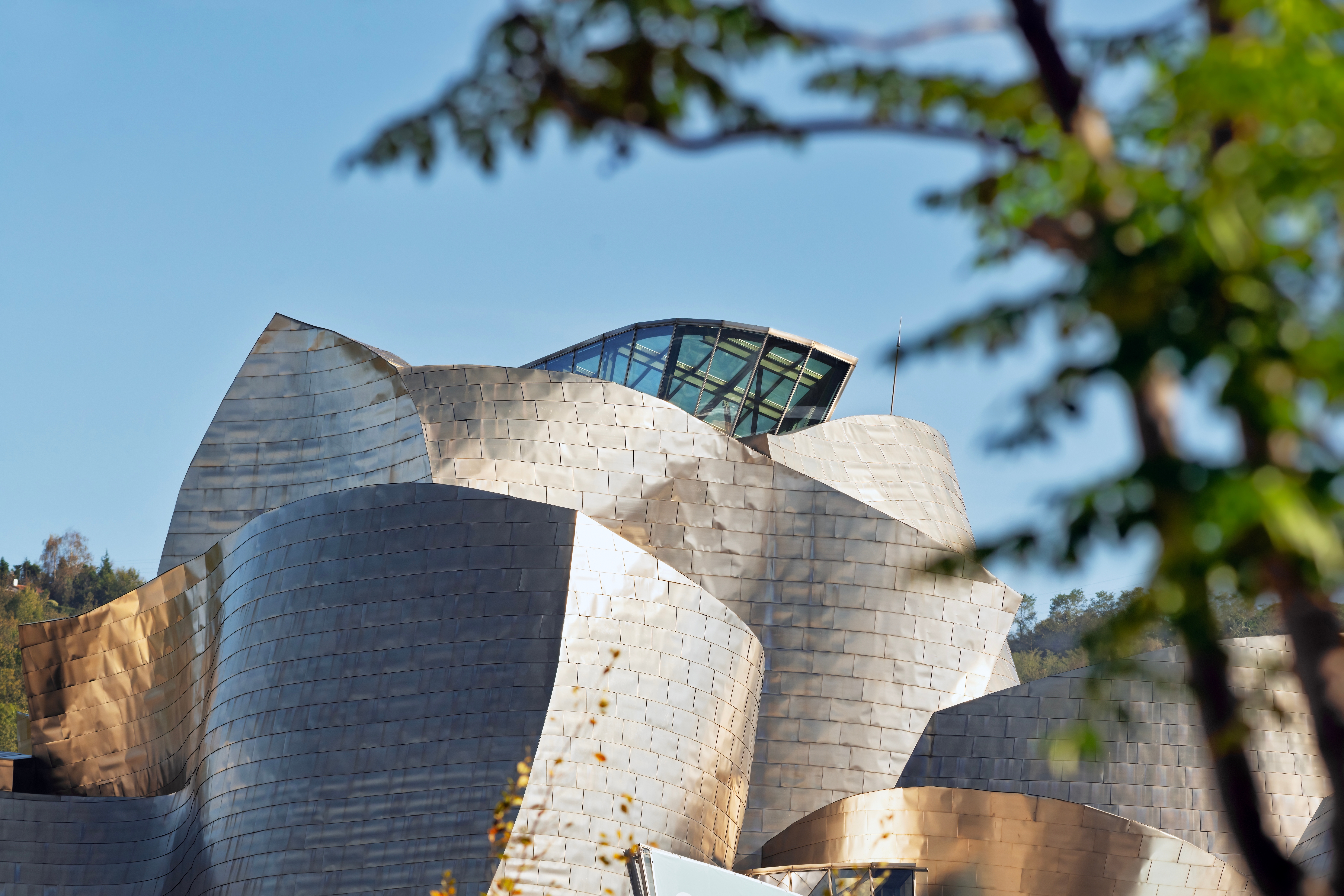 Guggenheim Museum Bilbao med ikonisk titaniumfacade og bølgende metallige kurver mod en klar blå himmel i Spanien