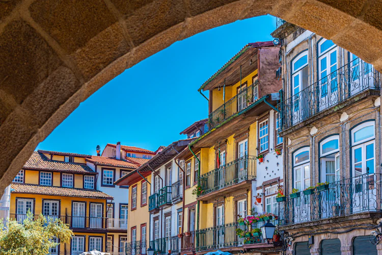 Farverige historiske bygningsfacader med smedejernsbalkoner ved Largo da Oliveira i den gamle bydel i Guimarães, Portugal