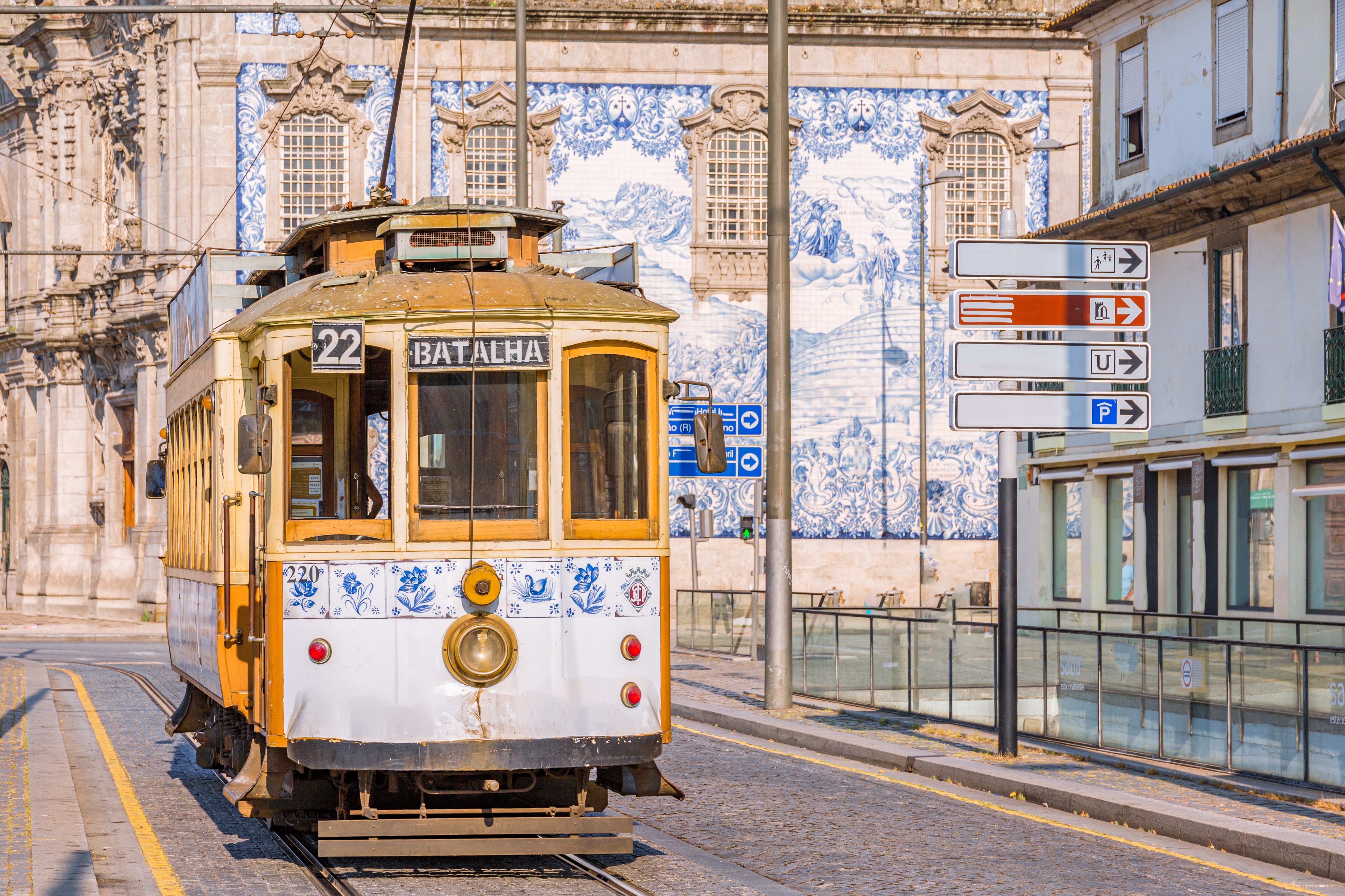 Historisk gul sporvogn nummer 22 mod Batalha foran smukke azulejo-flisedekorationer i Porto, Portugal