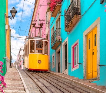 Traditionel gul sporvogn kører ned ad bakken i Lissabons historiske centrum med farverige bygninger og blomsterprydede altaner