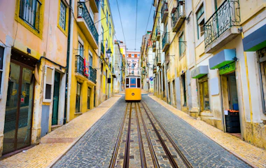Historisk gul sporvogn på brolagte gade i Lissabon Portugal med farverige bygninger
