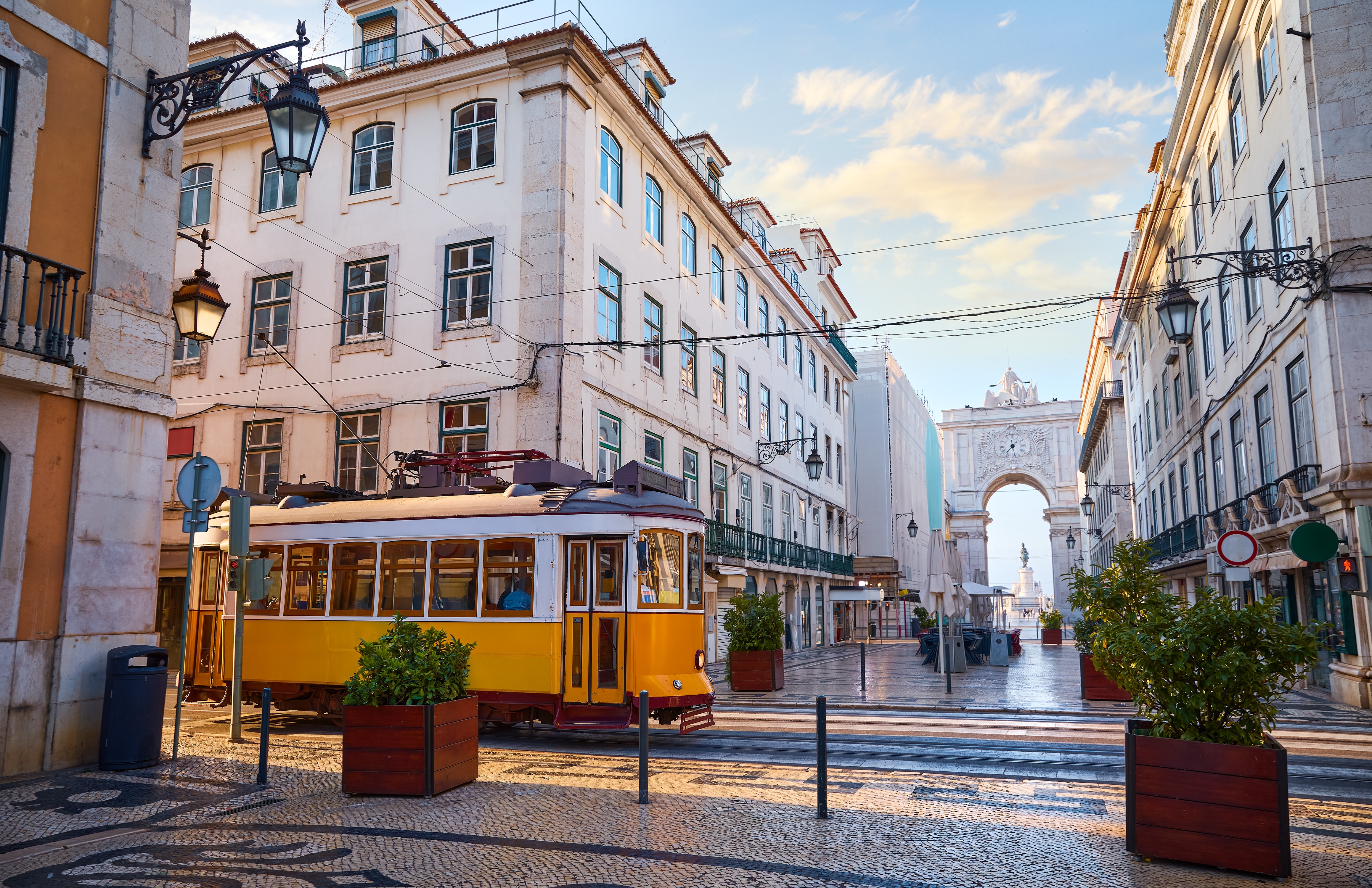 Gul retro sporvogn på brolagt gade i Lissabon med den triumfbue ved Rua Augusta og Praça do Comércio i baggrunden, Portugal