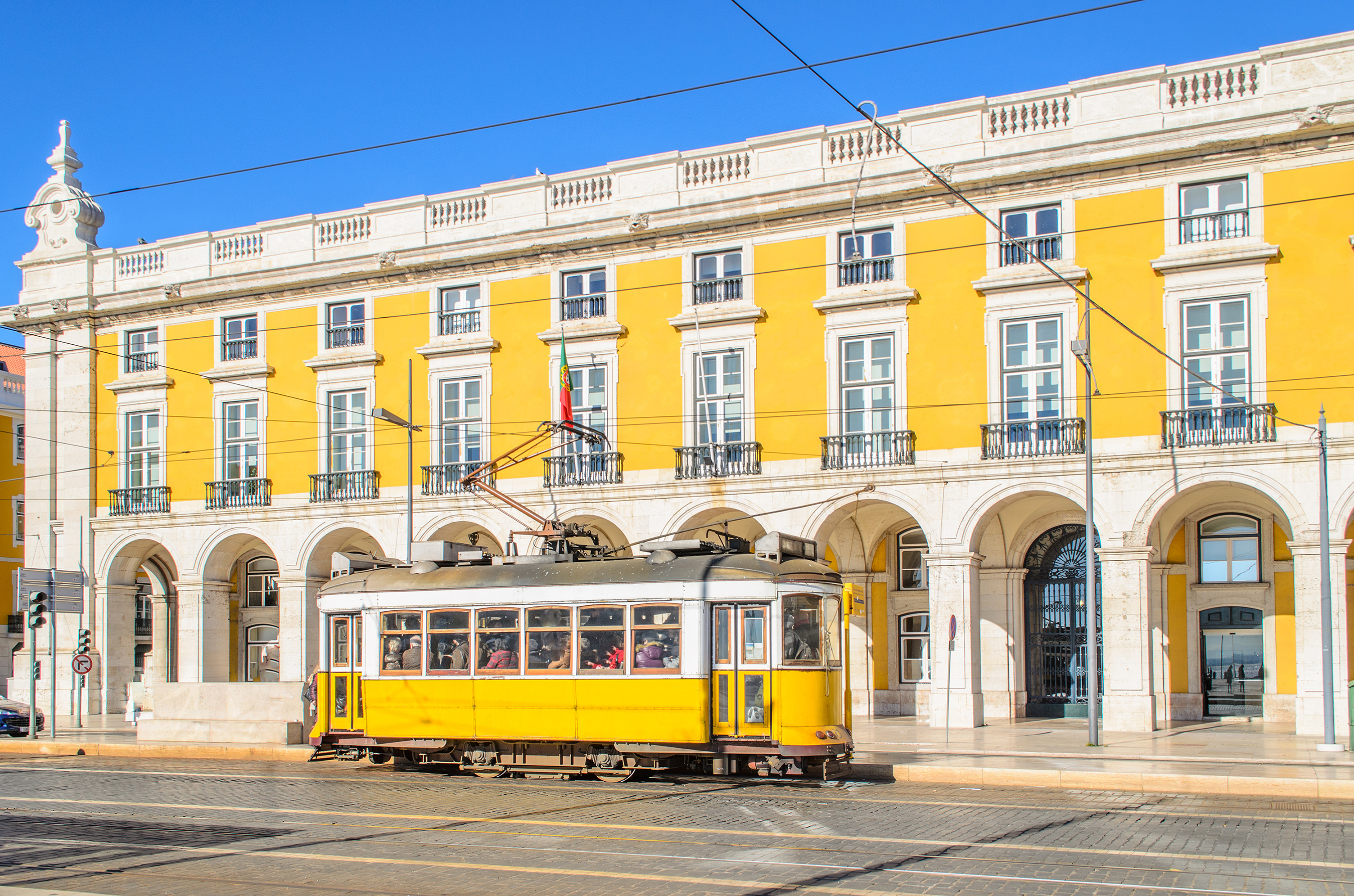Ikonisk gul sporvogn kører gennem den historiske Praça do Comércio plads med klassisk arkitektur i Lissabon, Portugal