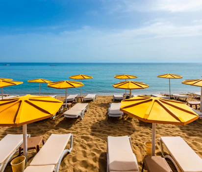 Smuk strand med gule parasoller og solsenge på sand ved klart blåt vand - perfekt feriested