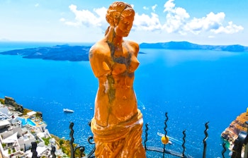 Gylden statue af Afrodite med panoramaudsigt over det blå Ægæerhav fra Santorinis caldera i Grækenland