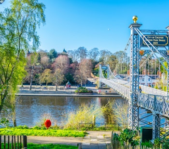 Malerisk udsigt over den historiske hængebro, der krydser floden Dee i Chester, med den smukke flodpromenade og refleksioner i det klare vand