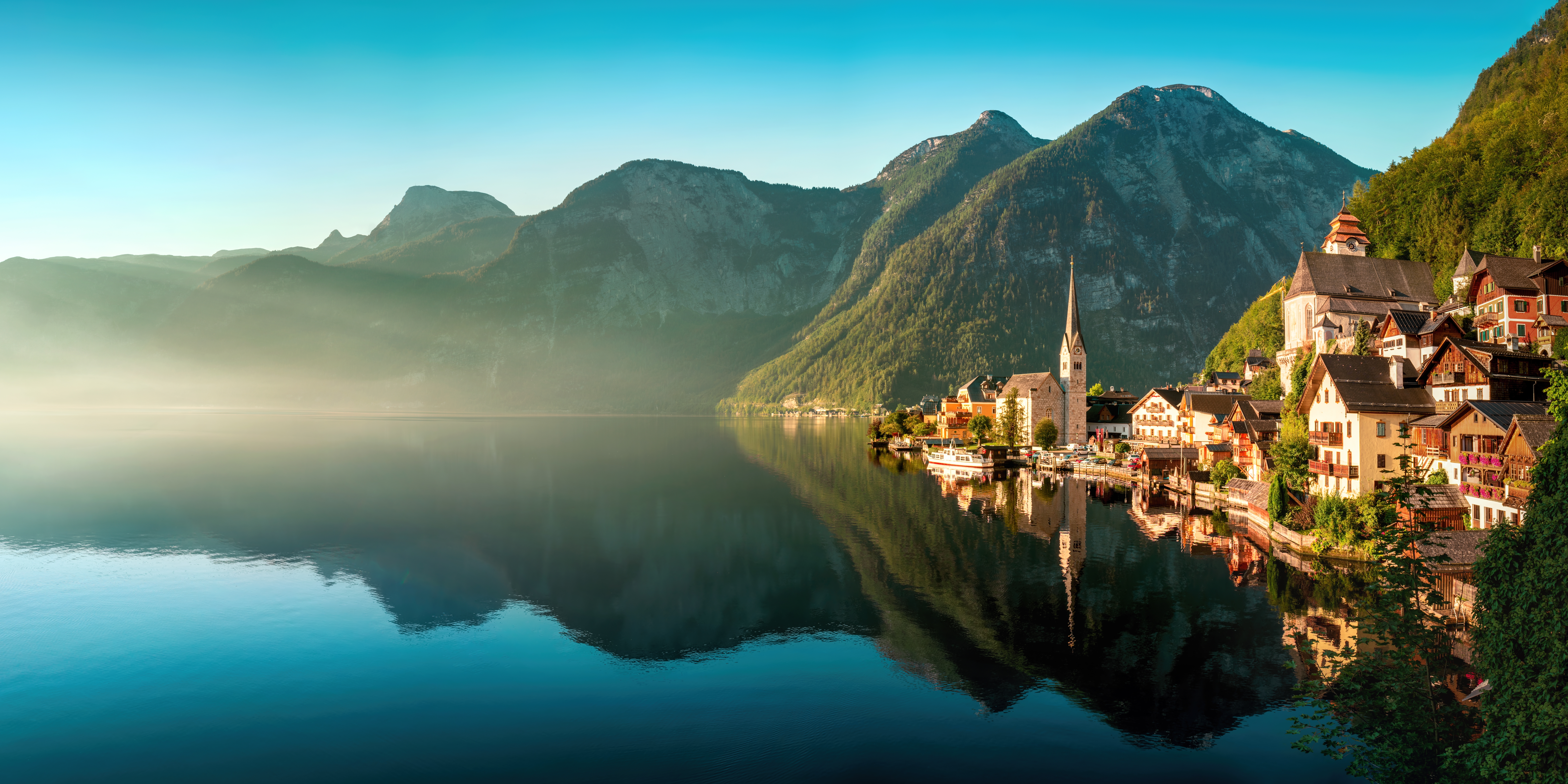 Hallstatt landsby i Østrig spejlet i rolig alpesø med tågede bjerge i baggrunden ved solopgang