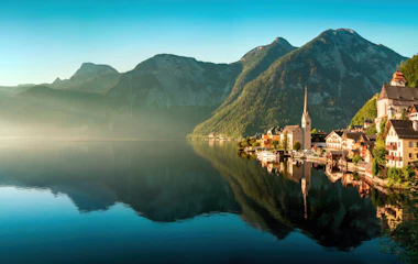 Hallstatt landsby i Østrig spejlet i rolig alpesø med tågede bjerge i baggrunden ved solopgang