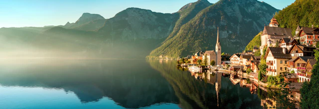 Hallstatt landsby i Østrig spejlet i rolig alpesø med tågede bjerge i baggrunden ved solopgang