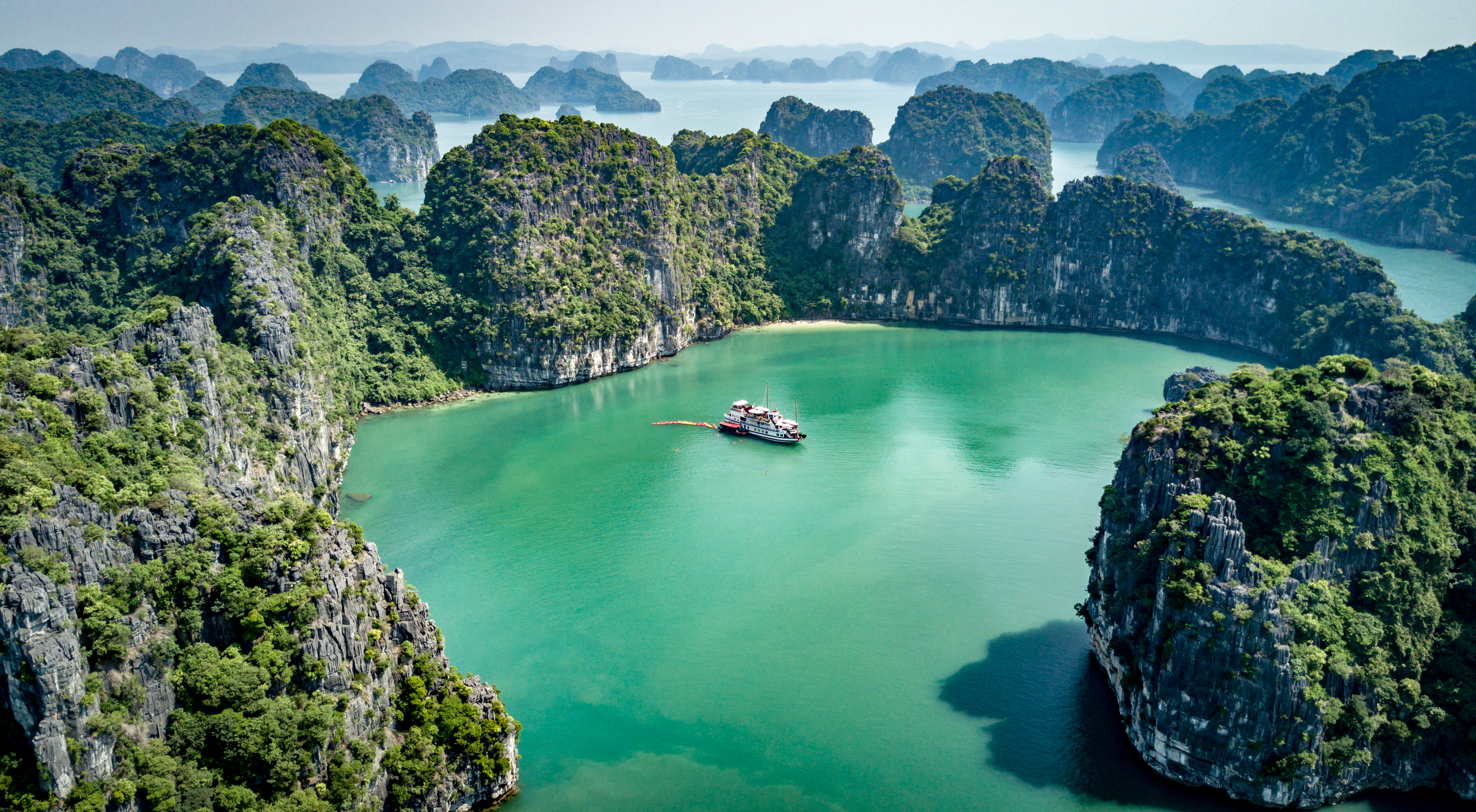 Krydstogtskib sejler gennem smaragdgrønne farvande i Halong Bay Vietnam med kalkstensøer