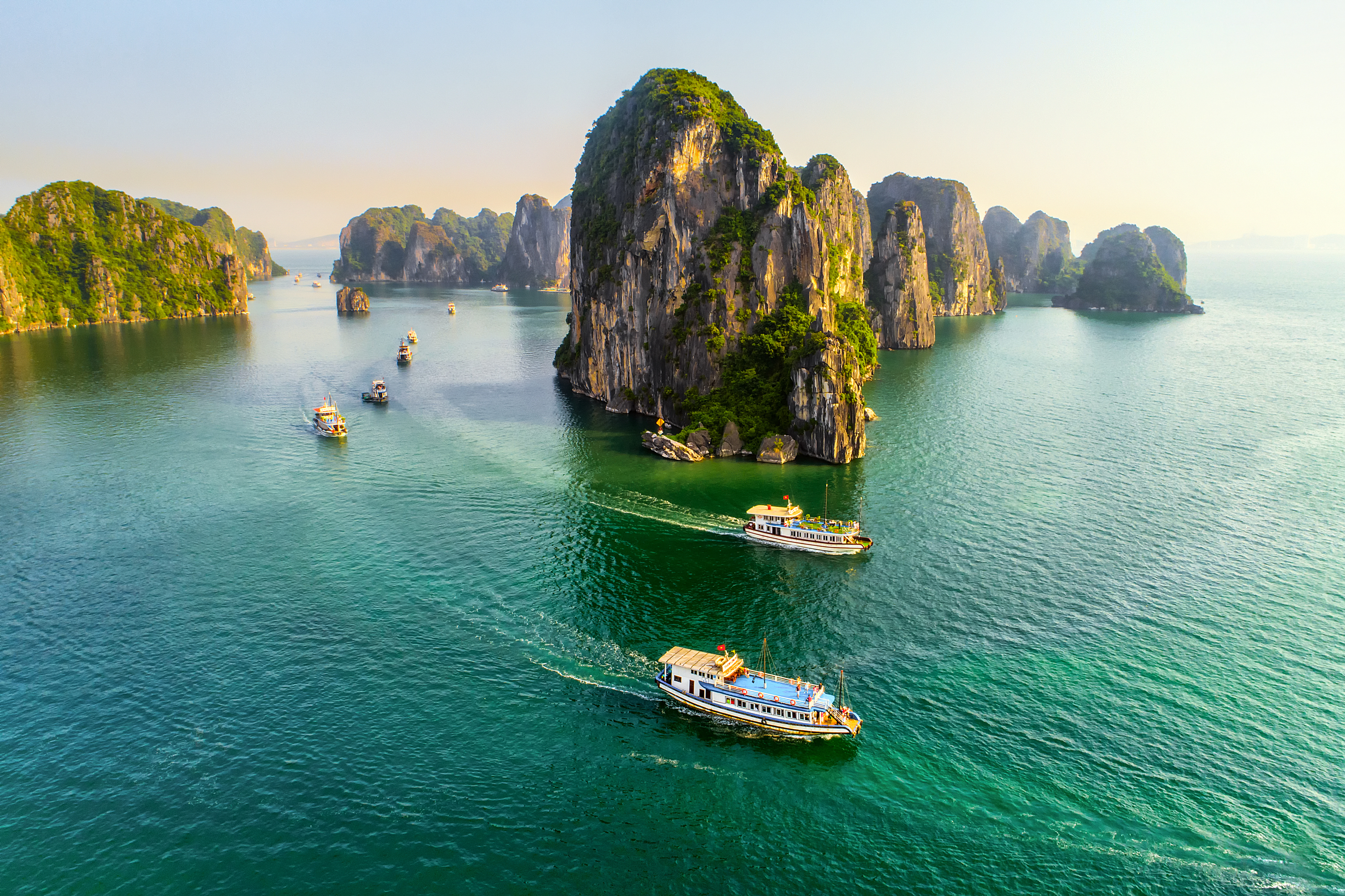 Spektakulære kalkstensklipper i Halong Bay Vietnam med smaragdgrønt vand og turistbåde der sejler mellem de majestætiske klippeformationer