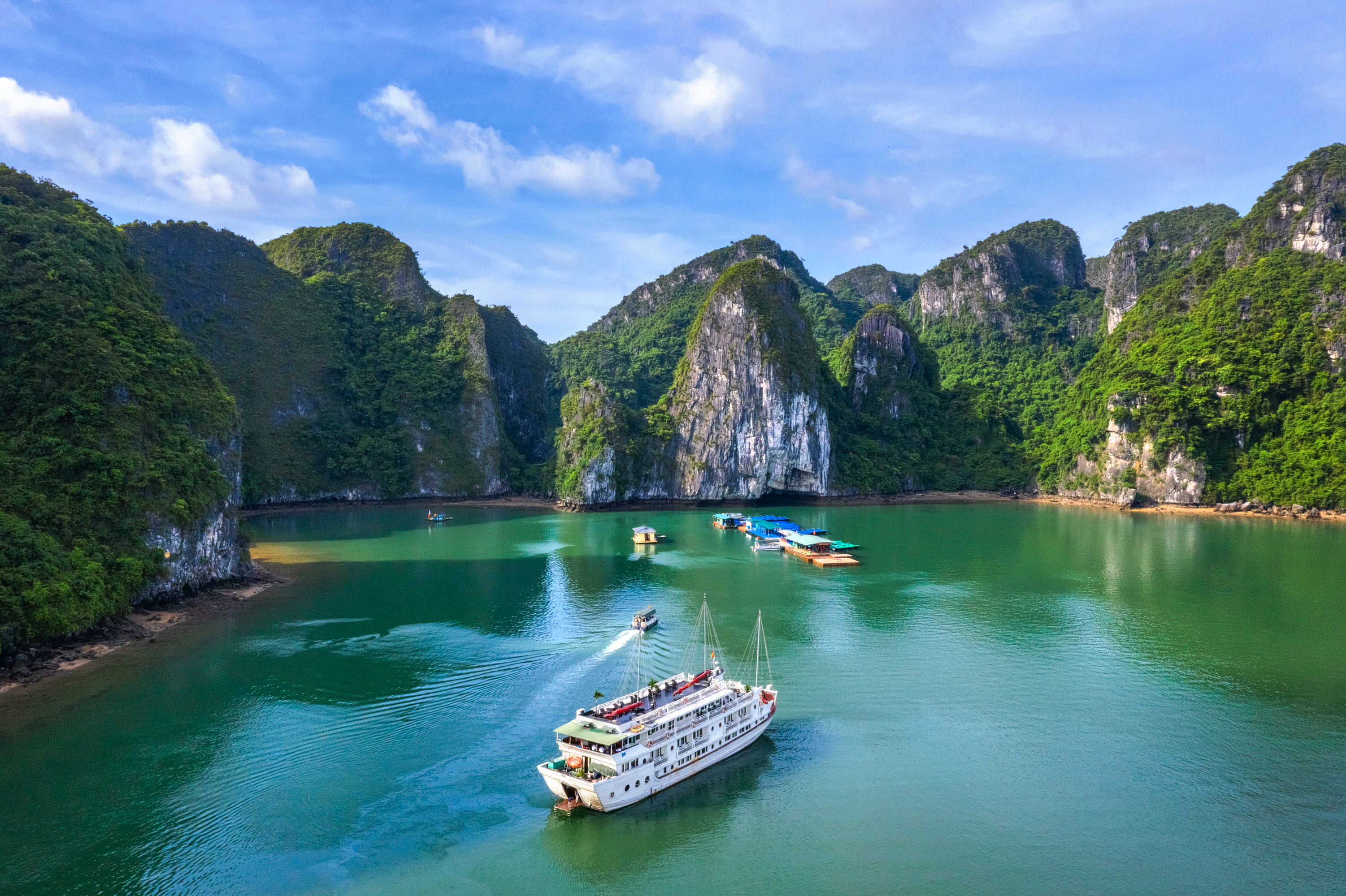Luftfoto af luksusskib på sejltur gennem Halong Bay i Vietnam omgivet af dramatiske kalkstensøer og smaragdgrønt vand