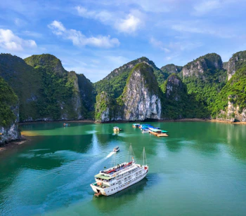 Luftfoto af luksusskib på sejltur gennem Halong Bay i Vietnam omgivet af dramatiske kalkstensøer og smaragdgrønt vand