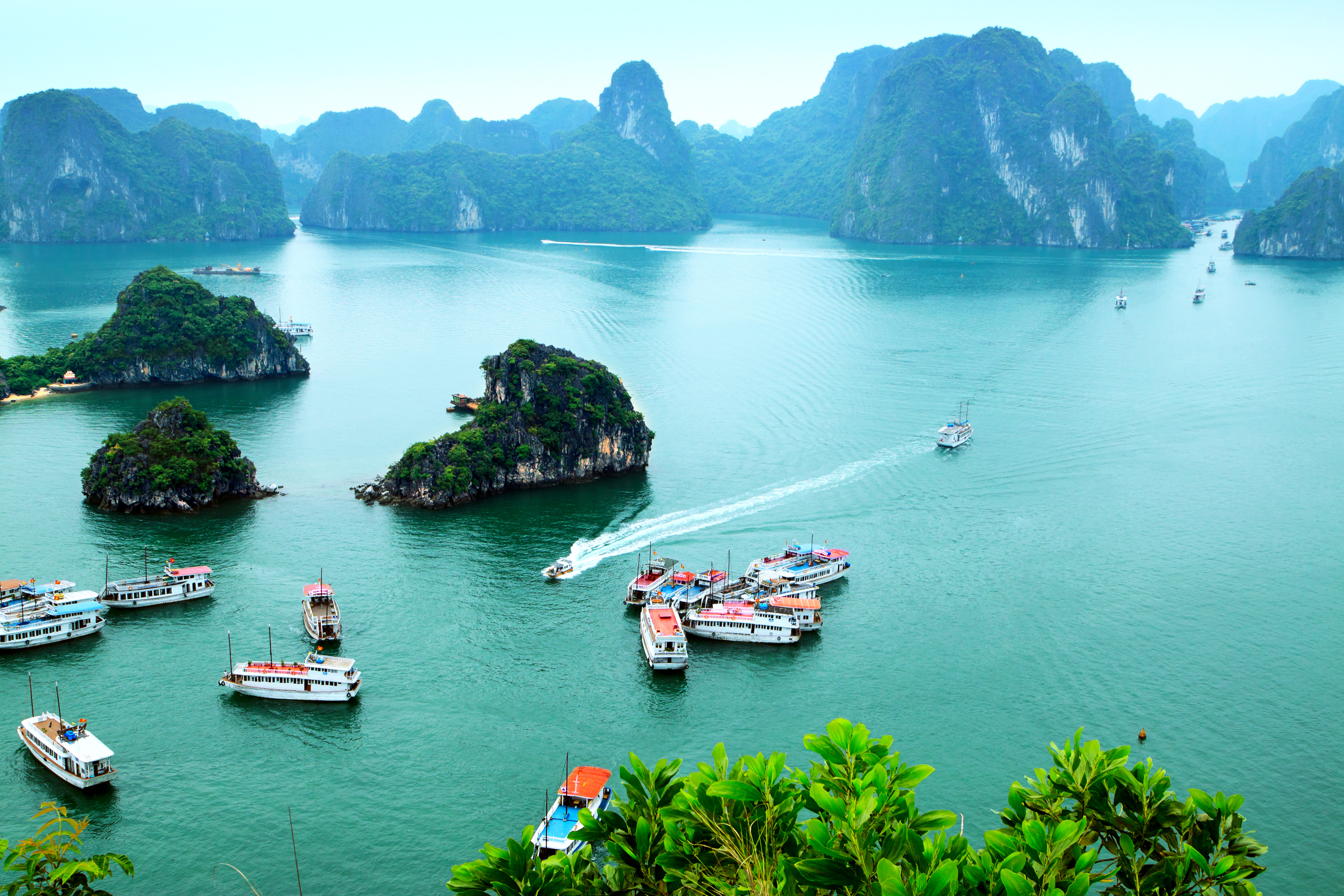 Traditionelle turistbåde sejler i Halong Bugtens smaragdgrønne vand omgivet af majestætiske kalkstensklipper i Vietnam