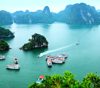 Traditionelle turistbåde sejler i Halong Bugtens smaragdgrønne vand omgivet af majestætiske kalkstensklipper i Vietnam