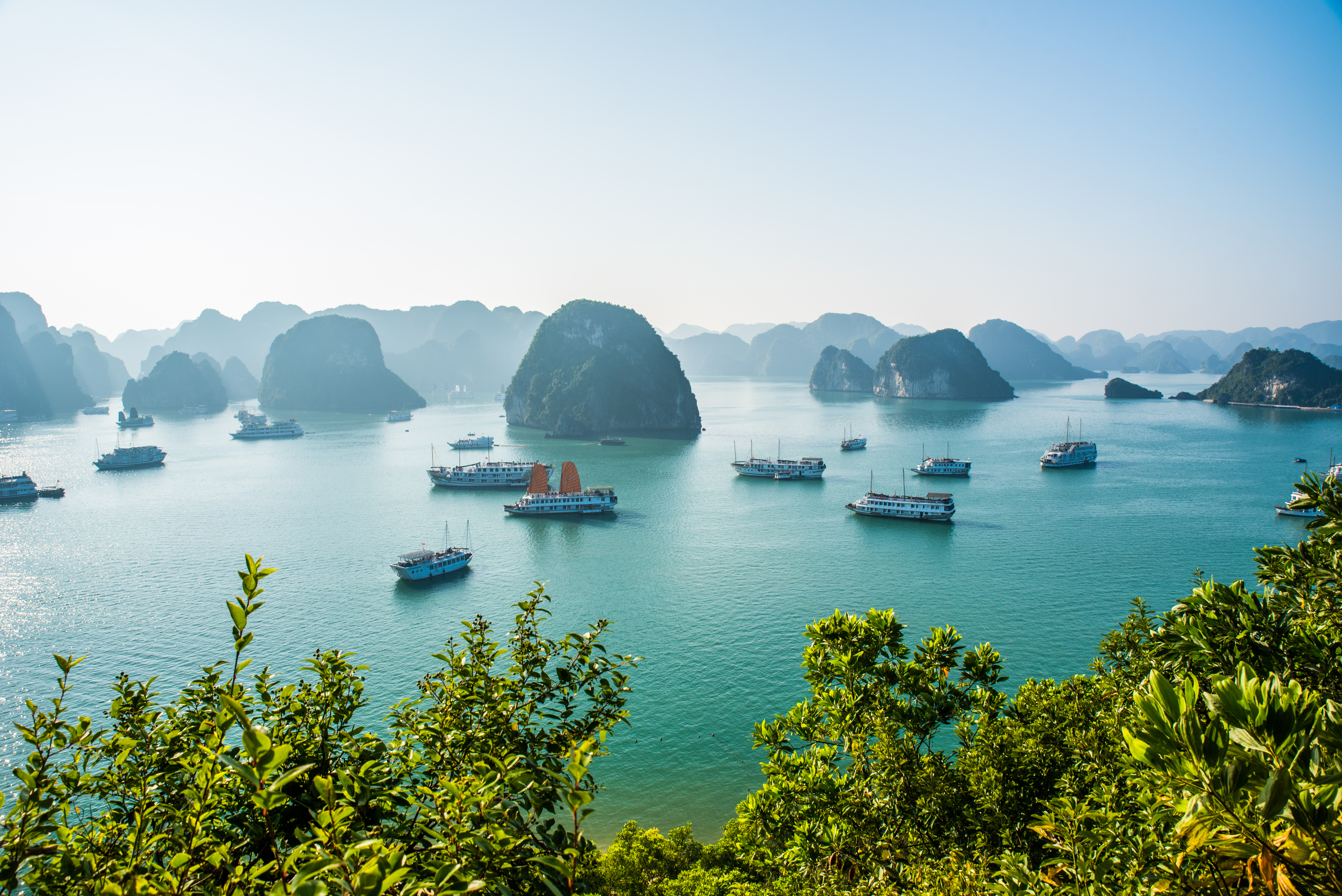 Panoramaudsigt over Ha Long Bugt i Vietnam med turkisblåt vand, dramatiske kalkstensøer og traditionelle krydstogtsbåde sejlende mellem imponerende klippeformationer