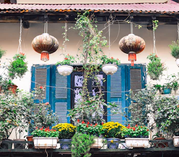 Charmerende traditionelt vietnamesisk byhus i Hanois gamle kvarter med blå træskodder, hængende lanterner og frodig blomsterdekoration på balkonen