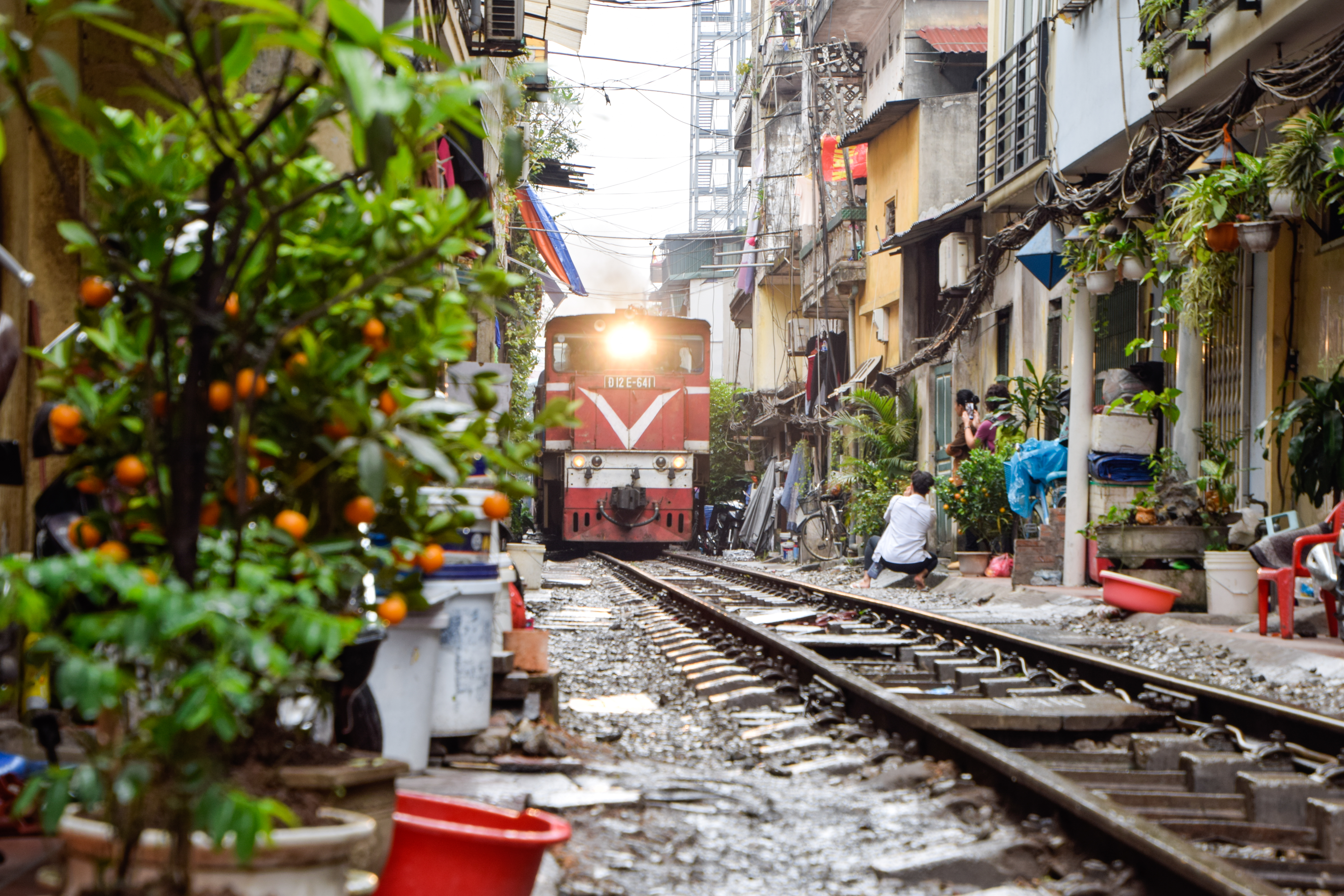 Rødt tog passerer gennem den berømte toggade i Hanoi, Vietnam, hvor jernbanen løber mellem tætpakkede huse og lokale beboere