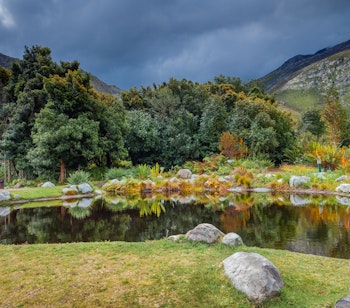Idyllisk sø omgivet af frodige bjerge i Harold Porter National Botanical Garden i Sydafrika, hvor den rige flora og naturskønhed skaber et betagende landskab