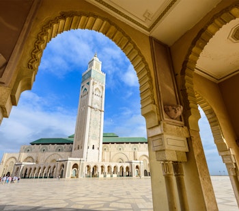 Den imponerende Hassan II-moské med sit høje minaret-tårn spejler sig i vandet ved solnedgang i Casablanca, Marokko