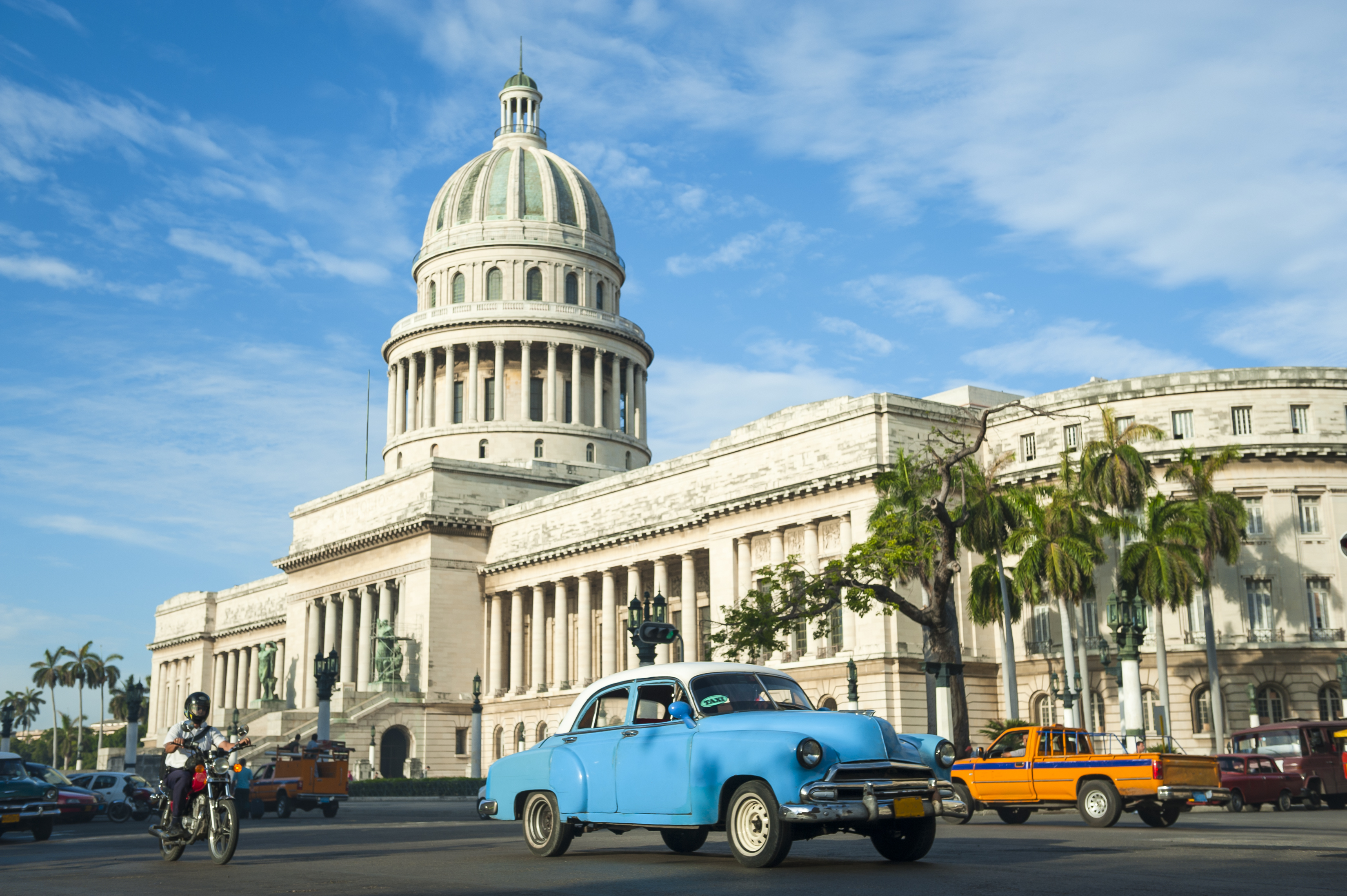 Klassisk blå veteranbil foran El Capitolio bygningen i Havana, Cuba med palmer og blå himmel