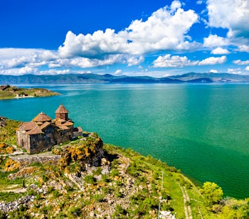Luftfoto af det historiske Hayravank kloster beliggende på bredden af Sevan-søen i Armenien med bjerglandskab i baggrunden