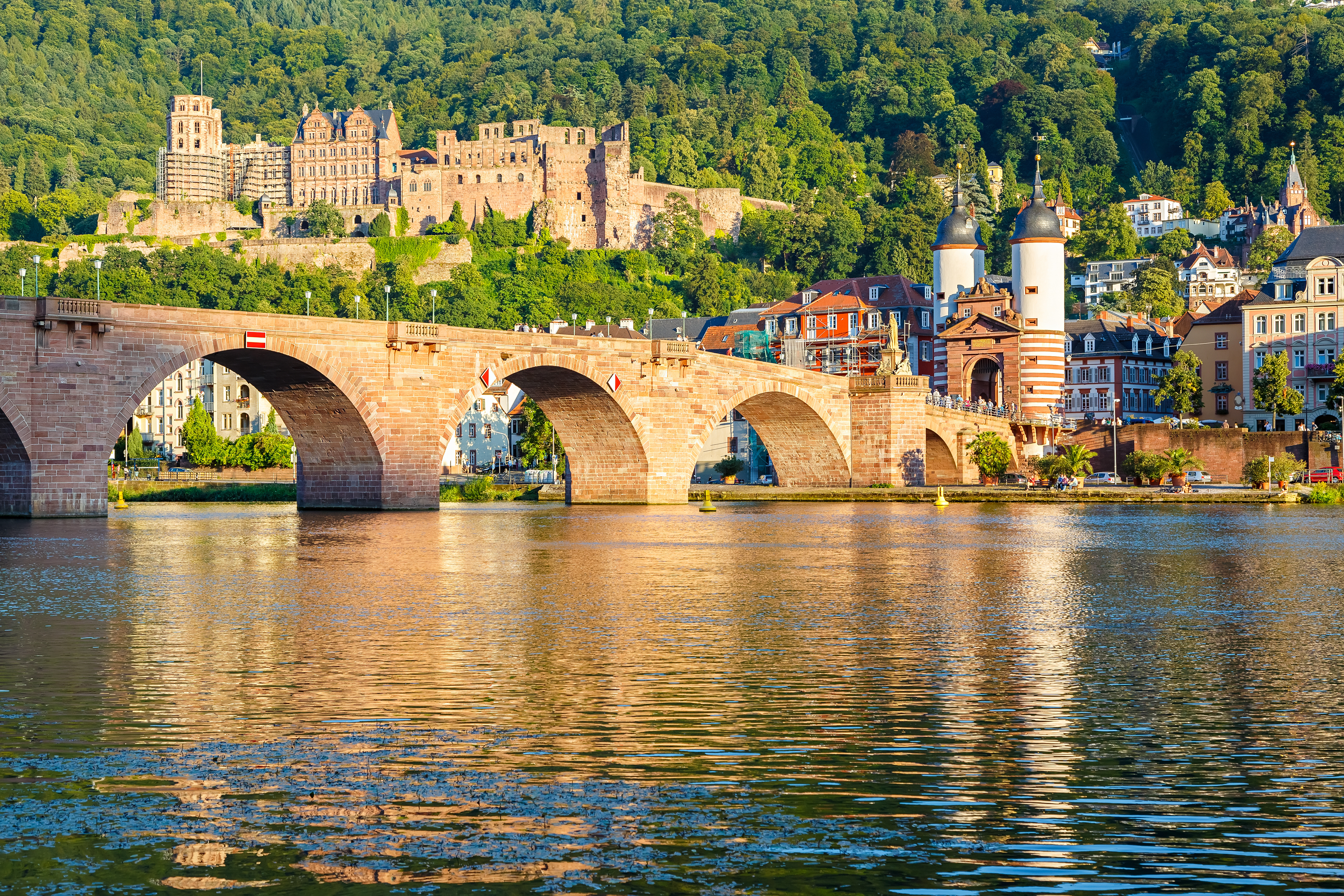 Den historiske Karl Theodor Bro i Heidelberg, Tyskland, med middelalderlige slotsruiner på bakken over Neckar-floden i gyldent aftenlys