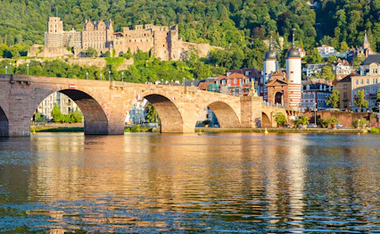 Den historiske Karl Theodor Bro i Heidelberg, Tyskland, med middelalderlige slotsruiner på bakken over Neckar-floden i gyldent aftenlys