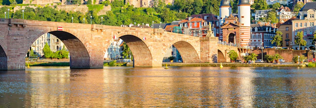Den historiske Karl Theodor Bro i Heidelberg, Tyskland, med middelalderlige slotsruiner på bakken over Neckar-floden i gyldent aftenlys