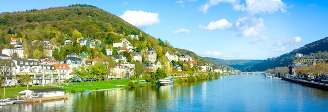 Panoramaudsigt over den historiske by Heidelberg med farverige bygninger langs Neckar-floden omgivet af grønne bakker i Tyskland