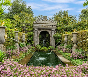 De smukke italienske haver ved Hever Castle i Kent, England, med klassisk stenbue, springvand og lyserøde blomster omgivet af grønne hække