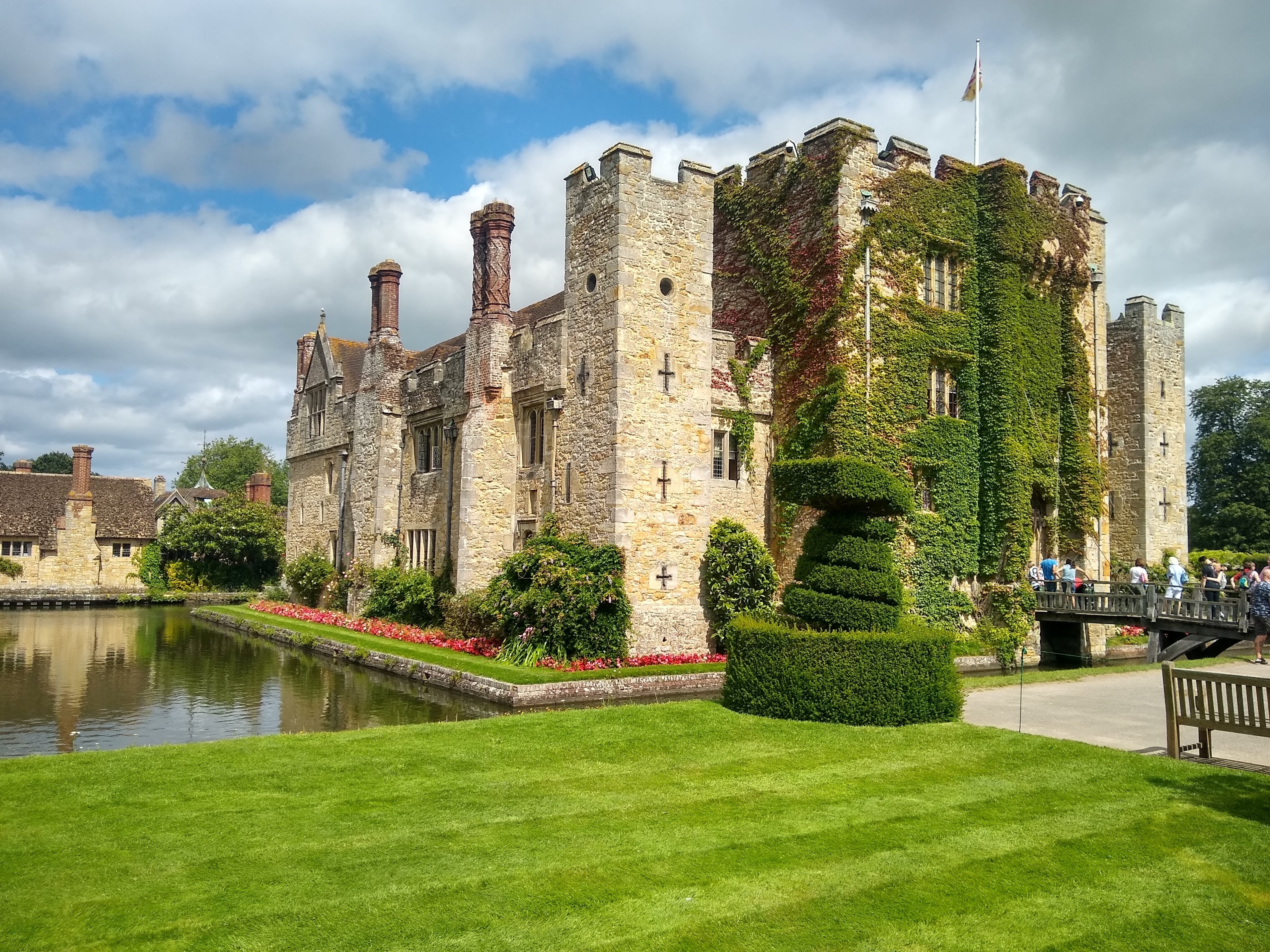 Hever Castle i Kent, England, dækket af vedbend med velholdte topiarhække, slotsgrav og besøgende på en solrig sommerdag
