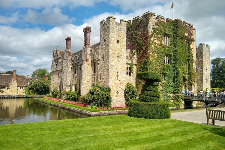 Hever Castle i Kent, England, dækket af vedbend med velholdte topiarhække, slotsgrav og besøgende på en solrig sommerdag