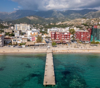 Luftfoto af den idylliske kystby Himare i Albanien med smuk sandstrand og krystalklart vand i det Ioniske Hav