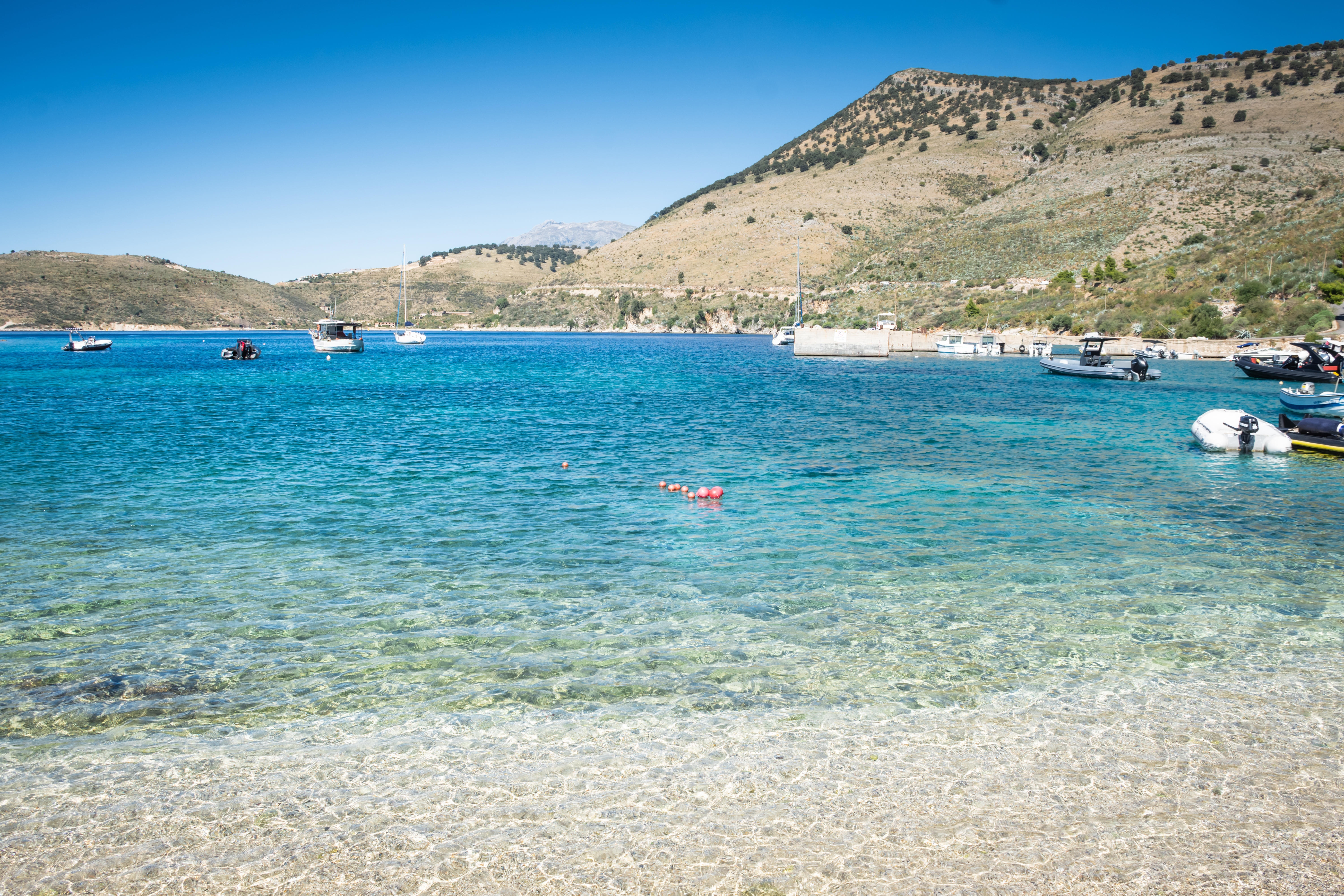 Krystalklart turkist vand i Himare Bugt Albanien med både forankret ved middelhavsstrand