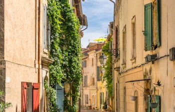 Malerisk smal gade i det historiske centrum af Arles i Provence - honningfarvede stenbygninger med grønne skodder og klatreplanter skaber den autentiske sydfranske stemning