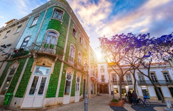 Idyllisk brostensbelagt gade i den gamle bydel i Lagos, Algarve, med traditionelle hvide bygninger og blå detaljer under solrig himmel