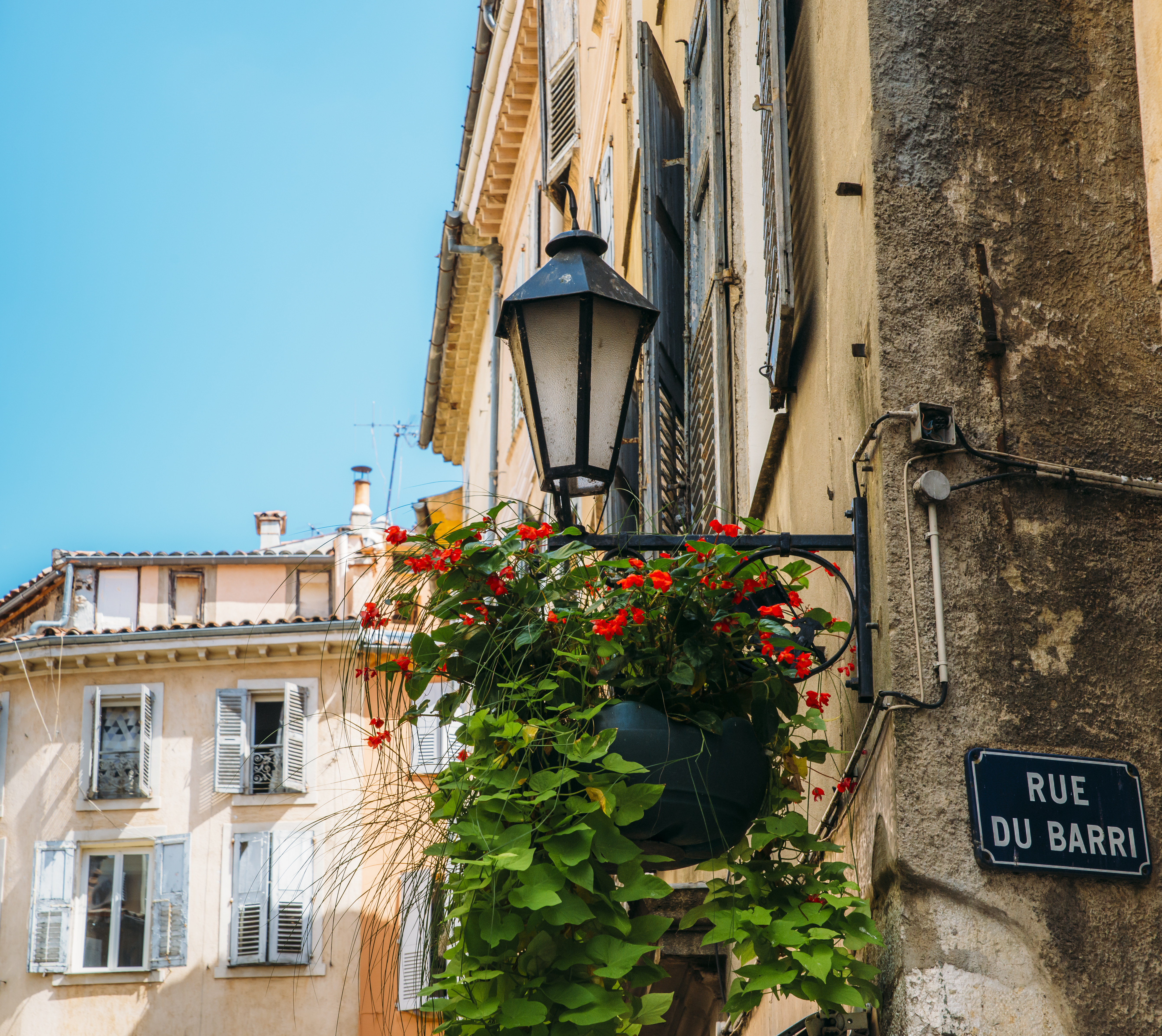 Charmerende historisk gadelampe med røde blomster i Grasse, den franske riviera