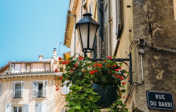 Charmerende historisk gadelampe med røde blomster i Grasse, den franske riviera