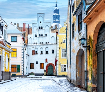 Snedækket brostensbelagt gade med historiske bygninger og regeringsmuseum i den middelalderlige gamle bydel i Riga, Letland