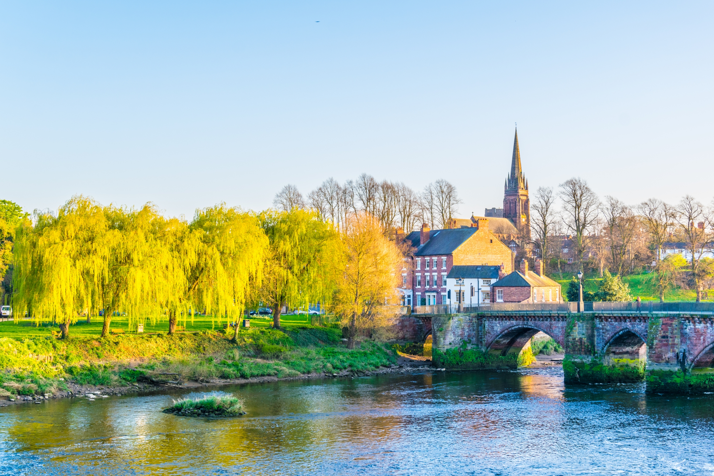 Den historiske Old Dee stenbro over floden i Chester, England med gule piletræer og kirkespir i baggrunden