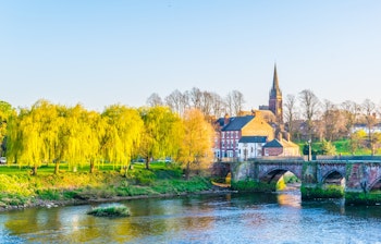Den historiske Old Dee stenbro over floden i Chester, England med gule piletræer og kirkespir i baggrunden