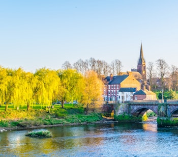 Den historiske Old Dee stenbro over floden i Chester, England med gule piletræer og kirkespir i baggrunden